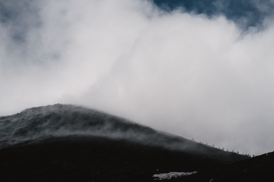 Dramatic view of a misty mountain slope enveloped by dense fog and clouds.