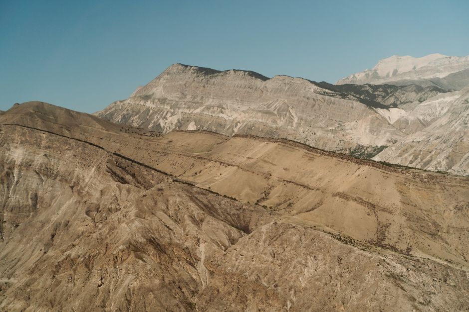 Aerial shot of rocky mountain terrain showcasing geological formations under clear blue sky.